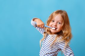 A little girl in striped pajamas is brushing her teeth with a toothbrush. The concept of daily hygiene. Isolated on a blue background